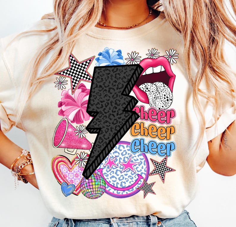 May include: Cream-colored sweatshirt with a graphic design featuring a black lightning bolt, pink lips, and the word "Cheer" in multiple colors. Other graphics include stars, hearts, and a disco ball.