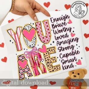 May include: A digital download featuring the words "YOU ARE" in a decorative font with pink hearts and gold accents. The words "Enough, Brave, Worthy, Loved, Amazing, Strong, Capable, Smart, Kind" are also displayed. A pink bow and hearts are also present.