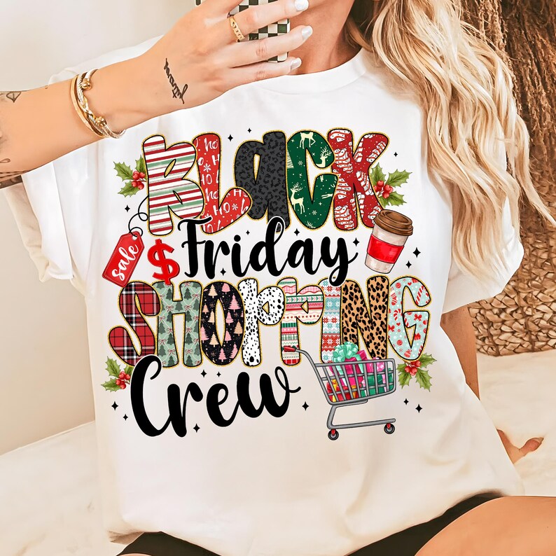 May include: White t-shirt with a colorful graphic that says "Black Friday Shopping Crew." The text features various patterns, including stripes, leopard print, and Christmas trees. A shopping cart filled with gifts is also included.