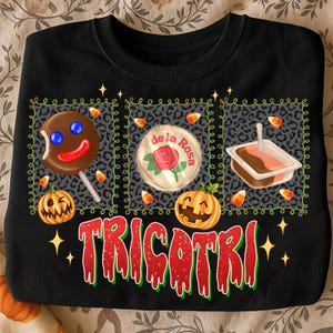 K&ouml;nnte beinhalten: Schwarzes Sweatshirt mit einem Halloween-Motiv. Das Design umfasst einen Lebkuchenmann-Lutscher, eine "de la Rosa" S&uuml;&szlig;igkeit und eine Dessertschale, alles innerhalb eines Leopardenmuster-Rahmens. Das Wort "TRICOTRI" ist in Rot und Gr&uuml;n geschrieben.