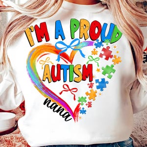 May include: White sweatshirt with a rainbow heart design and the text "I'm a proud autism nana". The heart is surrounded by puzzle pieces in various colors.