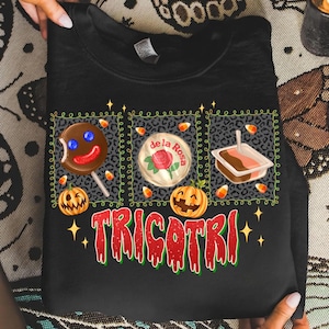 K&ouml;nnte beinhalten: Schwarzes Sweatshirt mit einem Halloween-Motiv. Das Design umfasst einen Lebkuchenmann-Lutscher, eine "de la Rosa" S&uuml;&szlig;igkeit und ein kleines Dessert, alles innerhalb eines Leopardenmuster-Rands. Das Wort "TRICOTRI" ist in Rot und Gr&uuml;n geschrieben.