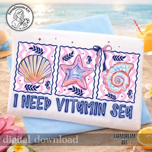 Pu&ograve; includere: Un telo da mare bianco con un disegno raffigurante una conchiglia, una stella marina e una conchiglia a spirale, ciascuna in un motivo ondulato rosa e bianco incorniciato. Il testo "I NEED VITAMIN SEA" &egrave; sotto le immagini. L'asciugamano &egrave; su un asciugamano blu su una spiaggia sabbiosa.