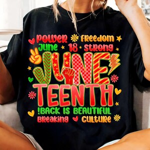 May include: Black t-shirt with a colorful graphic design celebrating Juneteenth. The design includes the words "Power," "Freedom," "June 18," and "Strong." The word "Juneteenth" is prominently displayed in red and green, with additional text: "Back is Beautiful, Breaking Culture."