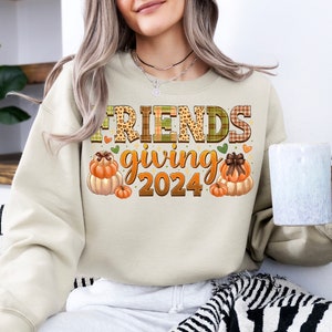 May include: A beige sweatshirt with the text "FRIENDS giving 2024" in a patchwork style with autumnal colours and pumpkins.