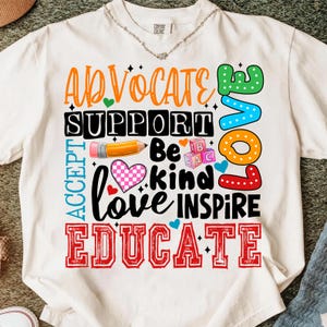 May include: White t-shirt with a colorful graphic design. The design includes the words "Advocate, Support, Accept, Love, Inspire, Educate" in various fonts and colors, along with a pencil, heart, and alphabet blocks.