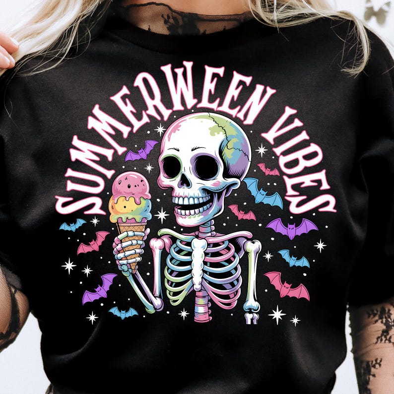 May include: Black t-shirt with a colorful graphic of a skeleton holding an ice cream cone. The text "SUMMERWEEN VIBES" arches above the skeleton. Bats and stars surround the skeleton, creating a spooky yet fun design.