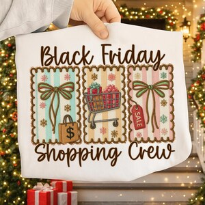 May include: White t-shirt with a festive design featuring the text "Black Friday Shopping Crew." The design includes three rectangular frames with bows, a shopping cart, a shopping bag, and a sale tag, all with a holiday theme.