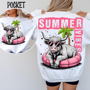 Op de afbeelding: Witte trui met een afbeelding van een Schotse hooglander die een zonnebril draagt en op een roze opblaasbaar zwembandje drijft. De tekst "SUMMER VIBES" staat op de achterkant van de trui.