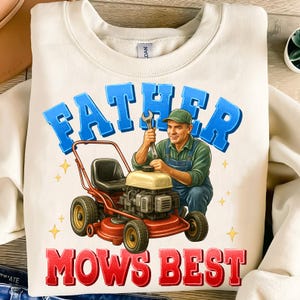 May include: Cream-colored sweatshirt with a graphic featuring a man working on a red lawnmower. The text "FATHER MOWS BEST" is in blue and red. The man is wearing a green cap and overalls.