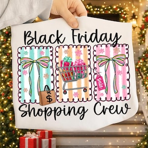 May include: White t-shirt with the text "Black Friday Shopping Crew". The design includes three rectangular panels with colorful striped backgrounds, bows, a shopping cart with gifts, and a shopping bag.