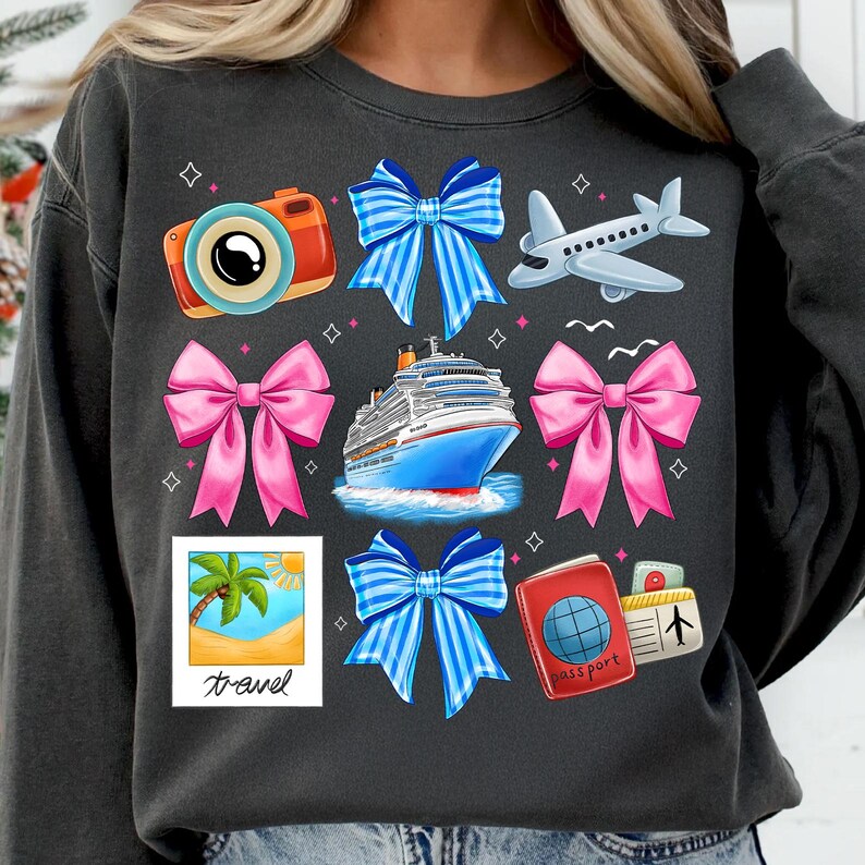 Puede incluir: Una sudadera gris oscuro con tem&aacute;tica de viaje. Presenta una c&aacute;mara, un crucero, un avi&oacute;n, una palmera, un pasaporte y varios lazos de diferentes colores.