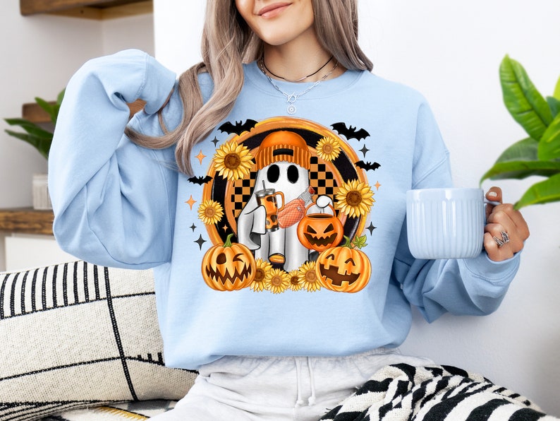 Peut inclure: Sweat-shirt bleu clair avec un motif d'Halloween. Le motif repr&eacute;sente un fant&ocirc;me portant un chapeau, tenant une boisson et une citrouille, entour&eacute; de tournesols, de chauves-souris et de citrouilles. Le sweat-shirt est de style d&eacute;contract&eacute; et confortable.