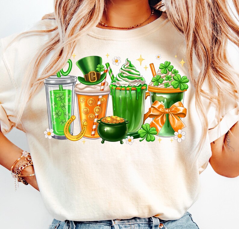 May include: White t-shirt with a graphic of four green, orange, and white drinks with shamrocks, a leprechaun hat, and a pot of gold.