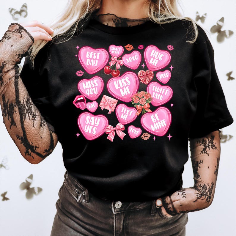 May include: Black t-shirt with pink heart-shaped candy designs. The candy hearts have various messages, including "Best Day", "Kiss Me", "Hug Me", "Sweet Talk", and "Be Mine".