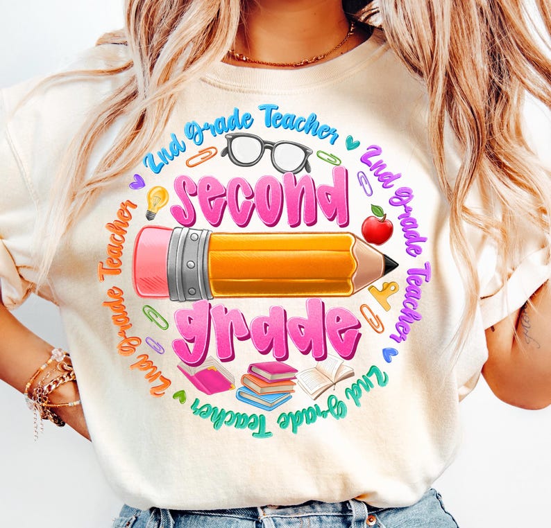 May include: Cream-colored t-shirt with a colorful graphic design for a 2nd-grade teacher. The design features a large pencil, the words "Second Grade" in pink, and other school-related elements like glasses, books, and an apple.