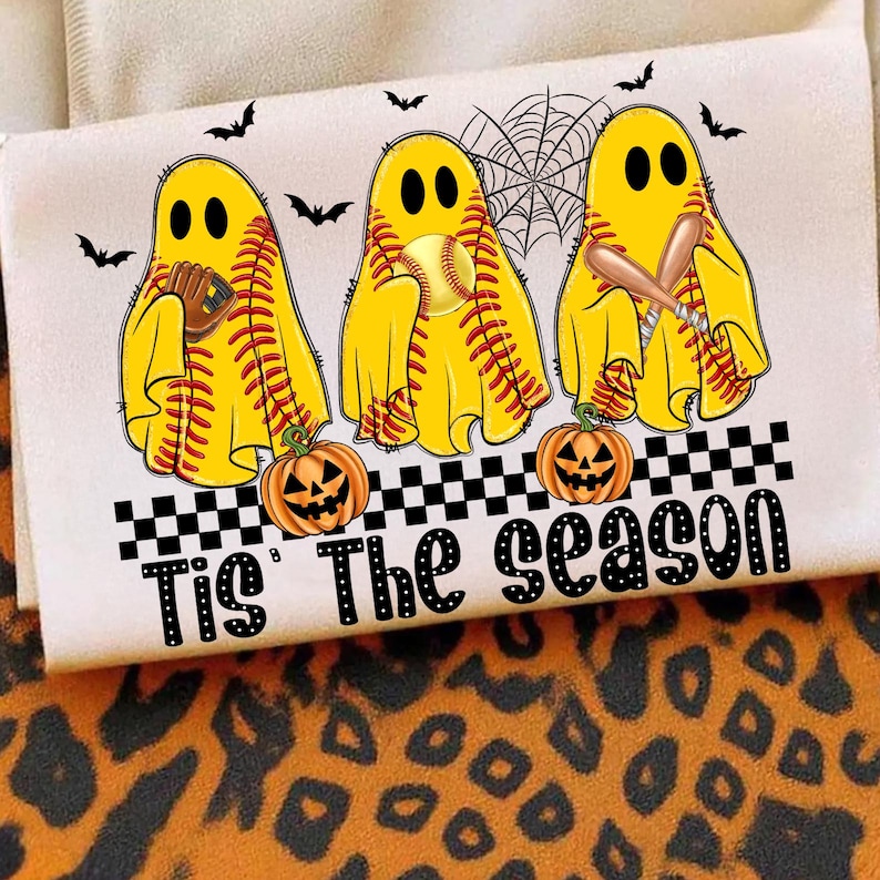 Puede incluir: Camiseta blanca con tres fantasmas amarillos con tem&aacute;tica de softbol, con bates, guantes y una pelota. La frase "Tis' The Season" est&aacute; impresa debajo de los fantasmas, con murci&eacute;lagos y calabazas. Tambi&eacute;n hay una telara&ntilde;a.