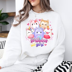 Puede incluir: Sudadera blanca con un gr&aacute;fico de cinco animales de dibujos animados, incluyendo un unicornio, un gato y una llama. El texto "birthday girl" est&aacute; impreso debajo de los animales.