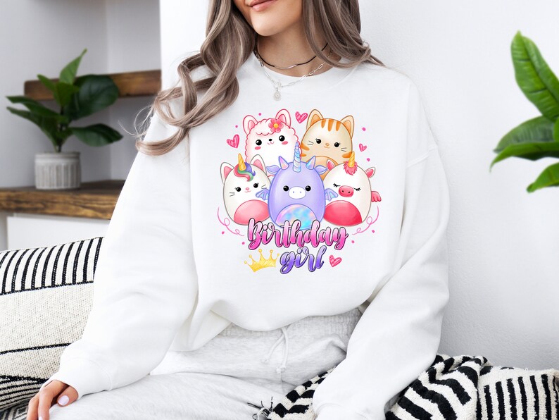Puede incluir: Sudadera blanca con un gr&aacute;fico de cinco animales de dibujos animados, incluyendo un unicornio, un gato y una llama. El texto "birthday girl" est&aacute; impreso debajo de los animales.
