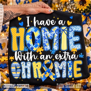 May include: A black t-shirt featuring the white text I have a HOMIE With an extra CHROMIE. The letters are decorated with yellow and blue patterns including puzzle pieces, ribbons, leopard print, stripes, and polka dots, with a blue ribbon.