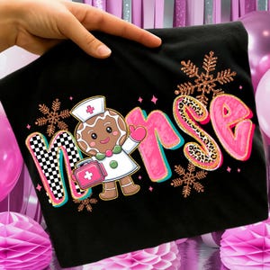 May include: Black t-shirt featuring the word "Nurse" with a gingerbread nurse graphic. The "N" has a checkered pattern, the "RSE" is pink with leopard print accents, and snowflakes are scattered around the design. The gingerbread nurse is holding a medical bag.