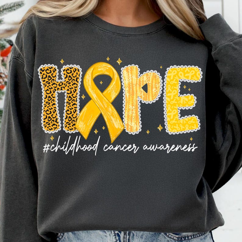 May include: Dark gray sweatshirt with the word "HOPE" in yellow and leopard print, with a yellow ribbon in the center. The text "#childhood cancer awareness" is written below the word "HOPE".