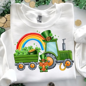 May include: A white sweatshirt with a green tractor pulling a wagon full of shamrocks and gold coins. A green leprechaun with a red beard and a green hat is standing in front of the tractor. A rainbow is in the background.