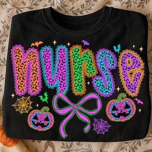 May include: Black sweatshirt with the word "NURSE" in colorful leopard print letters outlined with lace. The design includes bats, spiderwebs, a bow, and jack-o'-lanterns, all in a Halloween theme.