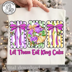 May include: White fabric with a colourful Mardi Gras design. The design features three rectangular frames with striped backgrounds in purple, green, and yellow. Each frame has a bow and a King Cake. Text reads "Let Them Eat King Cake."