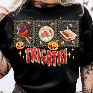 K&ouml;nnte beinhalten: Schwarzes T-Shirt mit einem Halloween-Motiv. Das Design zeigt einen Lolli, eine S&uuml;&szlig;igkeit und ein Dessert, jeweils vor einem Leopardenmuster-Hintergrund. Das Wort "TRICOTRI" ist in Rot und Gr&uuml;n geschrieben, mit K&uuml;rbissen und Zuckermais-Akzenten.