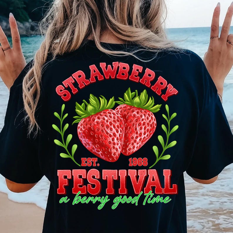 May include: Black t-shirt with a red and green graphic of two strawberries and the text "Strawberry Festival Est. 1968 a berry good time".