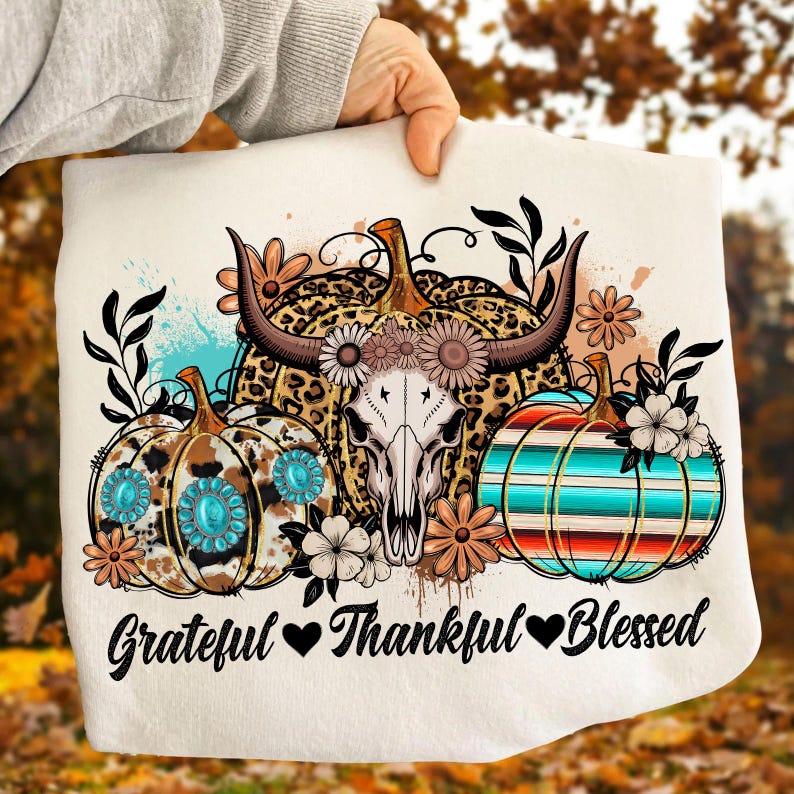 Puede incluir: Gr&aacute;fico color crema con tres calabazas con dise&ntilde;os florales y del suroeste. La calabaza central tiene una calavera con cuernos. El texto "Grateful, Thankful, Blessed" est&aacute; debajo.