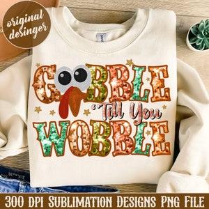 May include: A white sweatshirt with a Thanksgiving-themed design. The design features a cartoon turkey with the words "Gobble Till You Wobble" in colorful sequins.