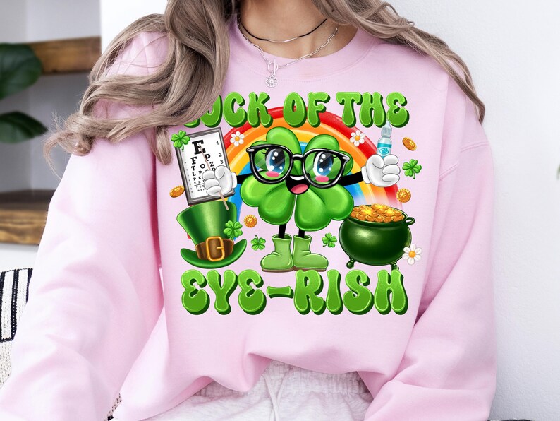 May include: Pink sweatshirt with a green shamrock cartoon character wearing glasses and holding an eye chart. The text "Luck of the Eye-rish" is printed on the shirt.