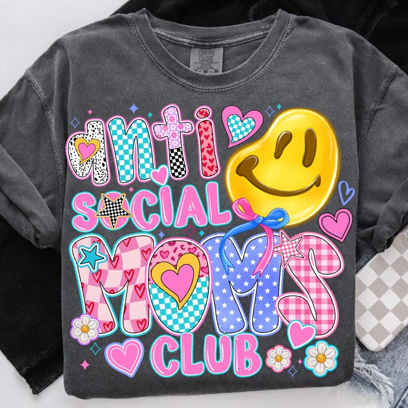May include: A gray t-shirt with a colorful graphic that says "Anti Social Moms Club". The graphic features a smiley face, hearts, stars, and checkered patterns.