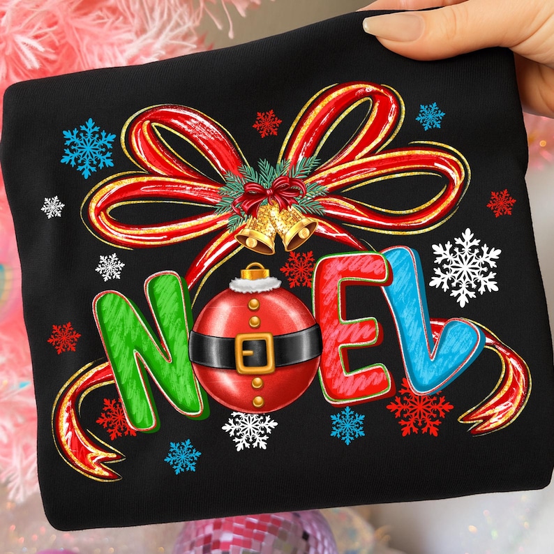 Pu&ograve; includere: Felpa nera con un design festivo. Presenta la parola "NOEL" in lettere verdi, rosse e blu, un ornamento rosso con cintura nera e un fiocco rosso con bordi dorati. Include fiocchi di neve e campane.