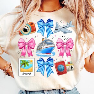 Puede incluir: Una camiseta blanca con un dise&ntilde;o de tem&aacute;tica de viaje. El dise&ntilde;o incluye un crucero, una c&aacute;mara, un pasaporte, un avi&oacute;n, palmeras y lazos en azul y rosa.