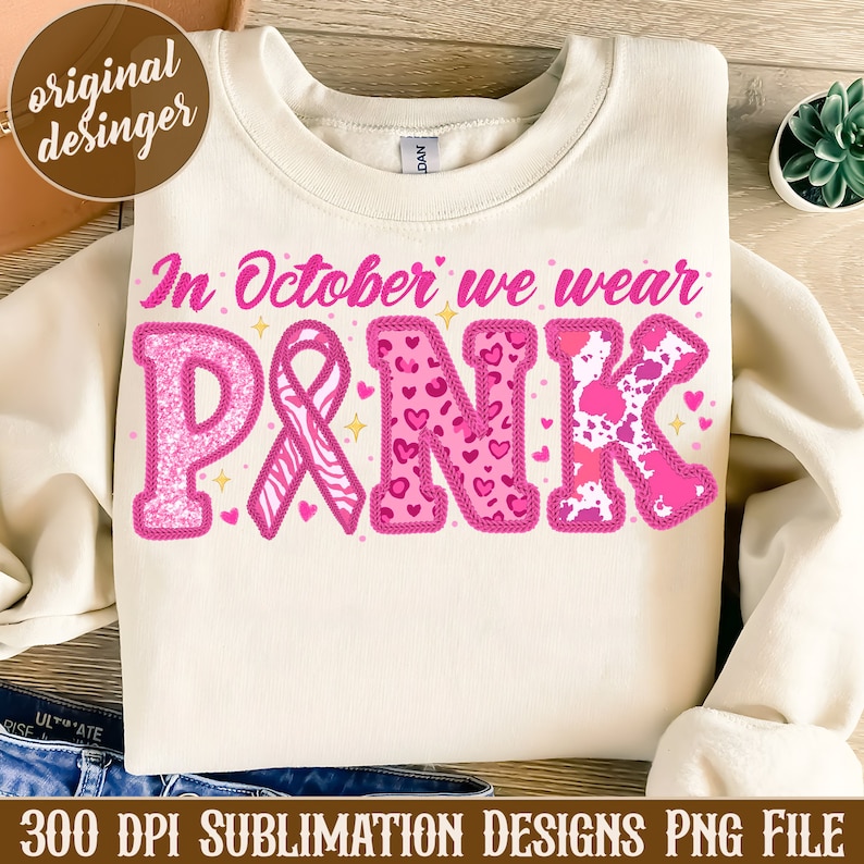 May include: A white sweatshirt with the text "In October we wear PINK" in pink letters. The letters are decorated with pink glitter, hearts, and animal print patterns. A pink ribbon is included in the design.
