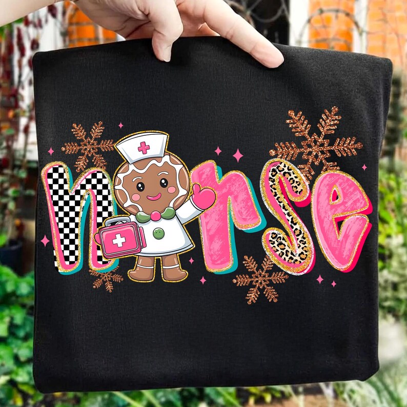 May include: Black sweatshirt with a colorful graphic that says "Nurse". The word "Nurse" is designed with a gingerbread nurse character, pink letters, and snowflake accents. The letter "N" has a black and white checkered pattern.