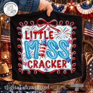 May include: Black t-shirt with a patriotic design. The shirt features the text "Little Miss Cracker" in red and blue, with a rocket and fireworks graphic. The design is framed by a red and blue border.