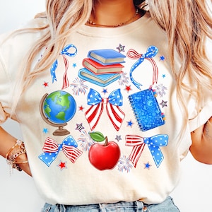 May include: A white t-shirt with a red, white, and blue design featuring a globe, books, a notebook, an apple, and bows. The design is perfect for teachers or students.