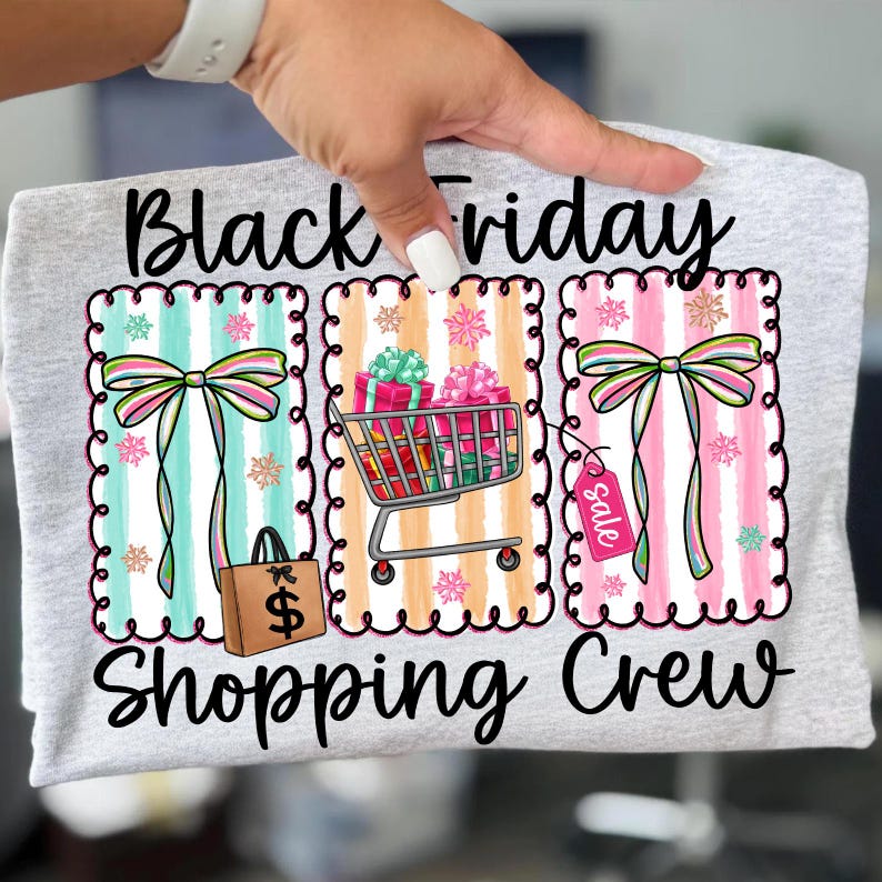 May include: A light gray t-shirt with the words "Black Friday Shopping Crew" in black script. The shirt features three colorful graphic designs with bows, shopping carts, gift boxes, and a sale tag.