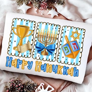 May include: White cushion with a blue and gold design featuring a gold trophy, menorah with a blue bow, and a dreidel. The words "Happy Hanukkah" are written in blue and gold.