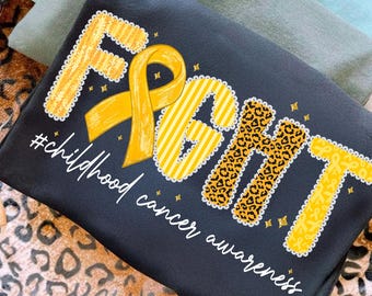 Może przedstawiać: Czarna koszulka z napisem "FIGHT" w kolorze żółtym, w panterkę i paski, z żółtą wstążką. Tekst "#childhood cancer awareness" jest napisany pod słowem "FIGHT".