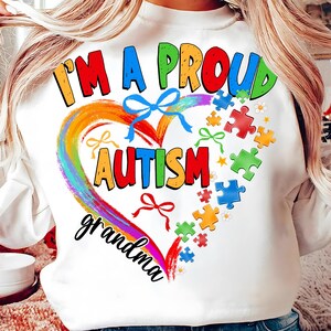 May include: White sweatshirt with a rainbow heart and the words "I'm a proud autism grandma". The heart is surrounded by puzzle pieces in various colors.