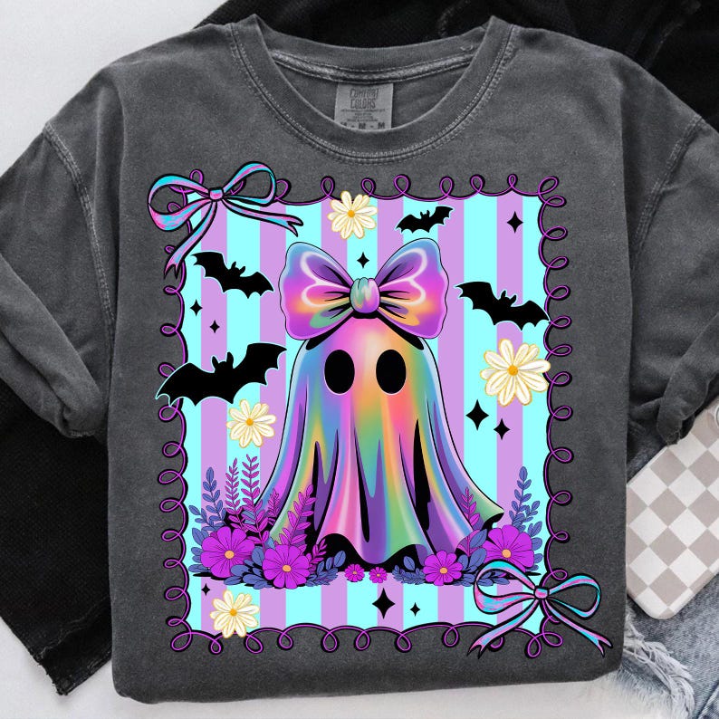 May include: Dark gray sweatshirt featuring a colorful ghost design. The ghost has a large bow and is surrounded by bats, flowers, and a striped background. The design is framed with a decorative border.