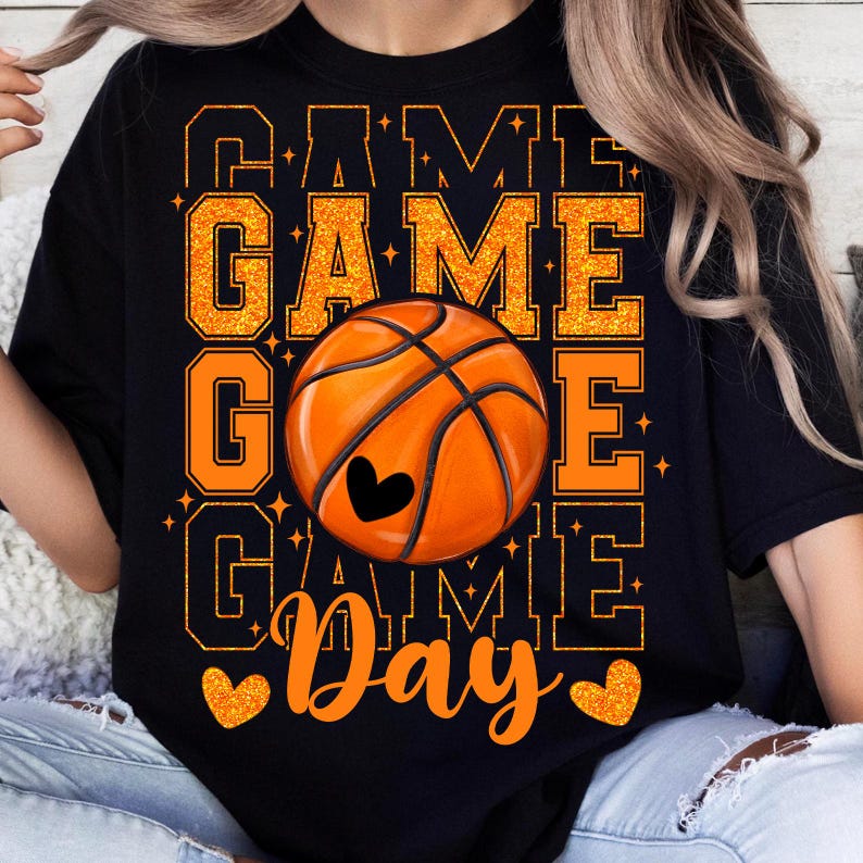 Peut inclure: T-shirt noir avec un texte en paillettes orange qui dit "Game Game Game Day" et un grand ballon de basket orange avec un c&oelig;ur au centre.