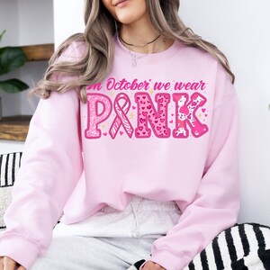 May include: Pink sweatshirt with the text "In October we wear PINK" in pink letters with glitter, hearts, and animal print designs.
