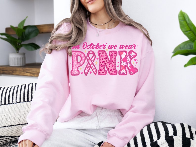 May include: Pink sweatshirt with the text "In October we wear PINK" in pink letters with glitter, hearts, and animal print designs.