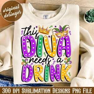 May include: A white sweatshirt with a purple, green, and yellow design that says "This Diva Needs a Drink". The design features polka dots, a crown, and a jester's hat.